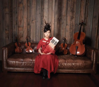 Hiromi Uehara on a couch with instruments, holding a keyboard.
